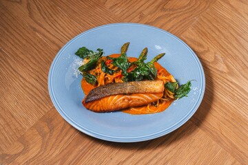 Grilled salmon fillet with red curry pasta and crispy Thai herbs on blue plate