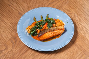 Grilled salmon fillet with red curry pasta and crispy Thai herbs on blue plate