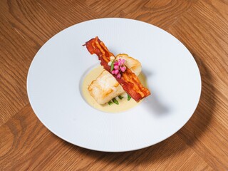 Snow fish with creamy sauce and crispy bacon on fine dining plate