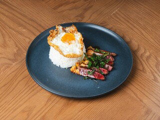 Thai beef basil with rice and crispy fried egg on black plate