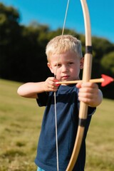 boy holding a bow and arrow in a field with trees in the background