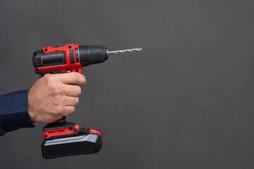 electric screwdriver in a man's hand, on a gray background.