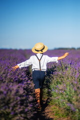 boy in a hat and shorts with suspenders runs into a field of lavender. Provence