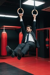 arafed man in a suit and tie hanging on rings in a gym