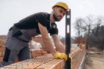 Using leveler tool. Construction worker is at job with bricks outdoors