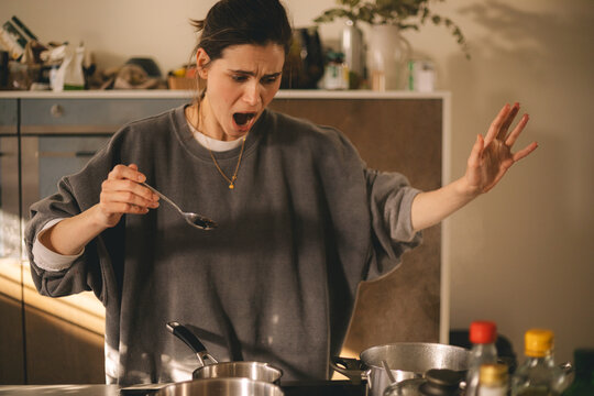 Young housewife having a calamity in the kitchen reacting in shock, she cooks dinner. Woman in a hurry, look sad and mad.