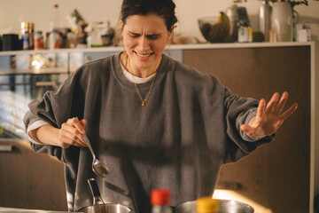 Young housewife having a calamity in the kitchen reacting in shock, she cooks dinner. Woman in a hurry, look sad and mad.