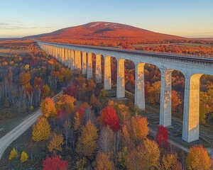 Long viaduct spans colorful fall foliage with a striking mountain backdrop. Use for travel articles, architecture, or autumn landscape themes.