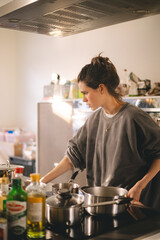 Woman standing by the stove in the kitchen, cooking and smelling the nice aromas from her meal in a pot. Housewife cooking lunch or breakfast.