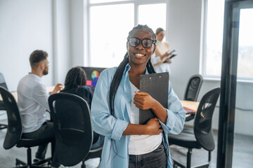 Woman is standing and smiling. Business people are working in the office