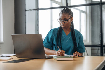 Silver colored laptop. Female doctor in coat is in the office clinic