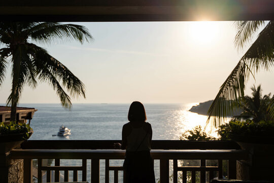 a silhouette of a lady standing by the veranda looking at the sunset by the sea