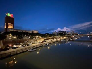 Fototapeta premium Cityscape of Pescara, Italy reflecting on the Pescara River at twilight with the City Hall and the Ponte Risorgimento bridge in the background