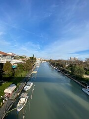 Naklejka premium Tranquil river winding through Pescara, wooden boats docked along banks, vibrant blue sky illuminating scenic urban landscape in Abruzzo, Italy