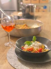 Traditional pasta featuring creamy burrata, ripe tomatoes, fresh basil garnish, served alongside classic spritz drink in rustic Abruzzo kitchen, capturing summer dining essence