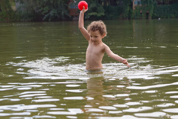 A curly child plays with a ball in the lake in the summer