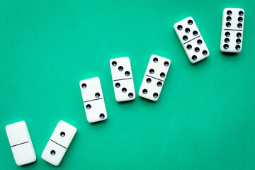 The game of dominoes is a table game involving rectangular pieces with dots that represent numbers. The objective is to match tiles with matching numbers. Photo with green background.