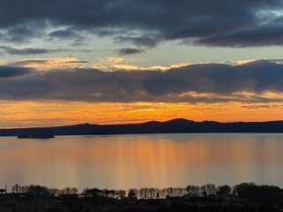 Sunset glow illuminating Bolsena Lake, casting warm hues on Bisentina Island, Mount Tabor looming...