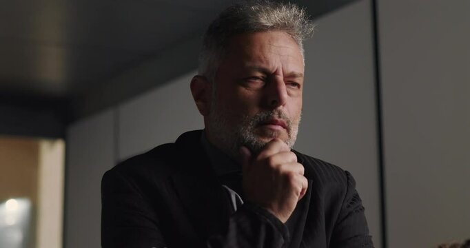 Pensive businessman lost in thought during corporate meeting with hand on chin and intense gaze in professional boardroom setting