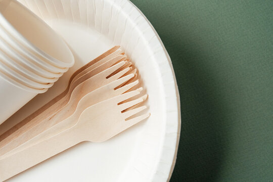 Disposable white paper cups and wooden forks on plate with green background