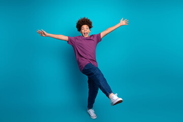 Fototapeta premium Happy teenage boy posing joyfully with open arms and a vibrant smile against a vivid blue background in casual attire