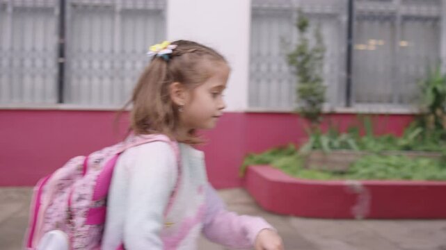 Schoolgirl with backpack showing paper fortune teller while walking outside school. The girl smiles playfully as she holds up the paper toy, enjoying her time