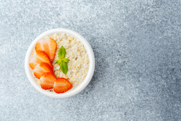 Strawberry oatmeal porridge with mint garnish in white bowl on gray surface