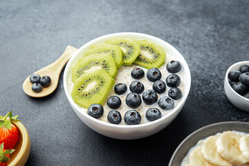 Oatmeal bowl with kiwi slices and blueberries next to strawberries and blueberries