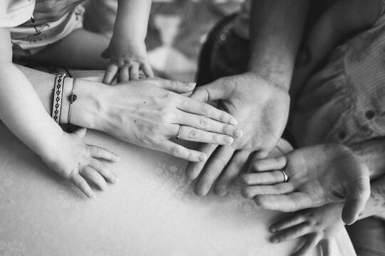 Black and white image showing a touching moment of unity and connection as multiple generations place their hands together, symbolizing family love and togetherness