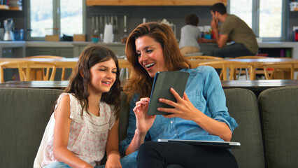 Mother And Daughter Sitting On Lounge Sofa Using Digital Tablet And Laptop