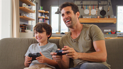 Father And Son Sitting On Sofa In Lounge At Home Playing Video Game