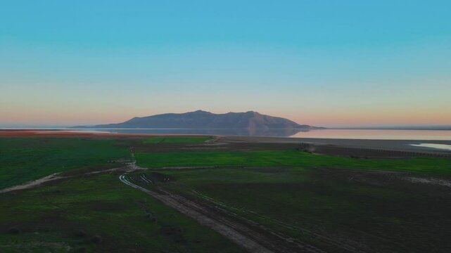 A captivating view of a tranquil coastal landscape featuring a vast body of water reflecting the sky, with green fields stretching into the distance, framed by a serene sunset or sunrise.
