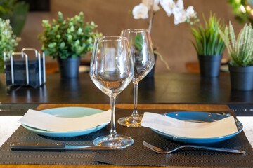 Empty wine glasses and tableware are set on a wooden table in a modern restaurant, creating a romantic atmosphere for an upcoming meal