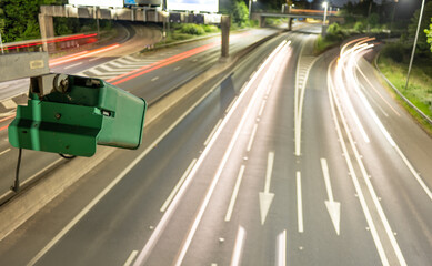ANPR vehicle surveillance. An ANPR camera on the motorway monitoring traffic flows and speed at night. Light trails of passsing vehicles can be seen,. 