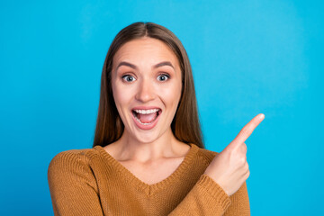 Happy young woman in casual attire pointing in excitement on a blue background, showcasing...
