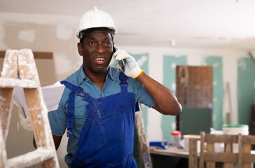 African american foreman working on a construction site indoors is talking to a colleague on a...