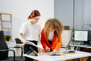 Women designers working on mobile app UX UI with color palettes, wireframes, and sticky notes....