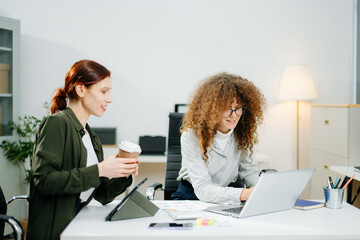 Two female professionals in smart casual outfits collaborate over finance charts and reports in a...