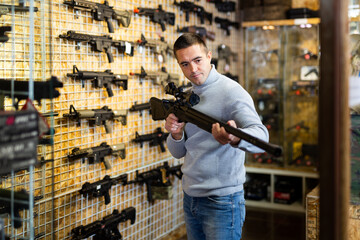 Man standing in showroom of weapon shop and choosing sniper rifle.