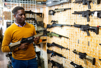 Portrait of active african american man choice pneumatic gun in airsoft market