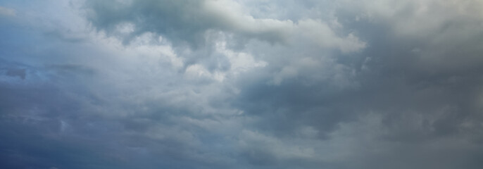 Fototapeta premium Dark storm clouds gather across the blue sky during the rainy season, forming dramatic shapes as nature signals an approaching storm over the open landscape.