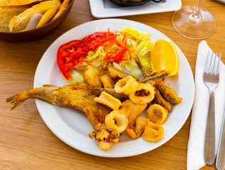 Healthy dinner of fried squid rings and fish with vegetable garnish and lemon slice