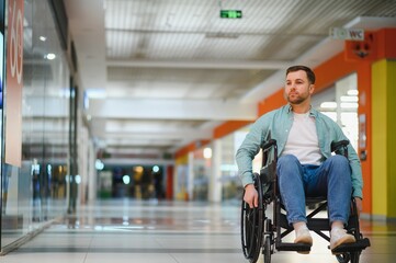 Person with disability sitting in wheelchair moving in shopping mall corridor