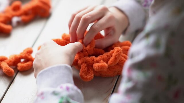 Teenage girl's hands stitching a handmade toy with white plush yarn and a plastic needle. Children's hobby. The girl sits holding a woolen thread in her hands.