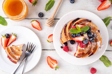 Sweet summer bundt cake with fresh fruit and berry. Traditional round sponge cake, seasonal dessert with strawberry, raspberry, blueberry, honey and sugar sprinkles, white wooden table copy space