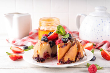 Sweet summer bundt cake with fresh fruit and berry. Traditional round sponge cake, seasonal dessert with strawberry, raspberry, blueberry, honey and sugar sprinkles, white wooden table copy space