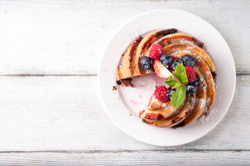 Sweet summer bundt cake with fresh fruit and berry. Traditional round sponge cake, seasonal dessert with strawberry, raspberry, blueberry, honey and sugar sprinkles, white wooden table copy space