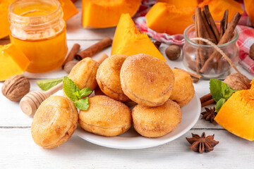 Autumn pumpkin pie donuts with cinnamon sugar sprinkled topping and pumpkin spice filling, on white wooden table with honey and pumpkin squash slices, copy space