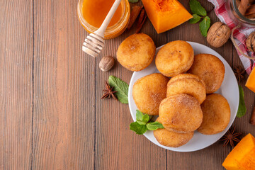 Autumn pumpkin pie donuts with cinnamon sugar sprinkled topping and pumpkin spice filling, on white wooden table with honey and pumpkin squash slices, copy space