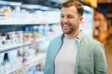 Fototapeta premium Smiling customer choosing products in supermarket refrigerator section